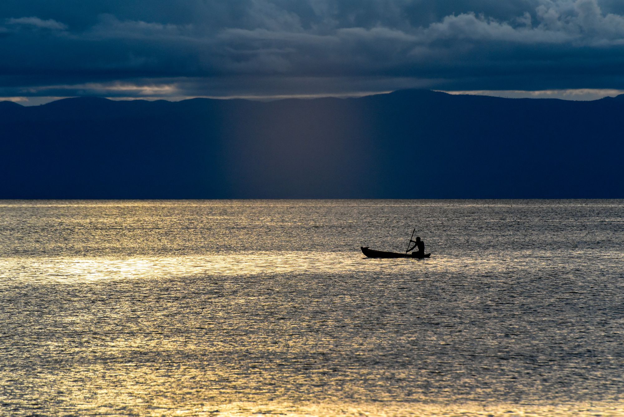 A lone canoe on the lake under a shaft of storm light