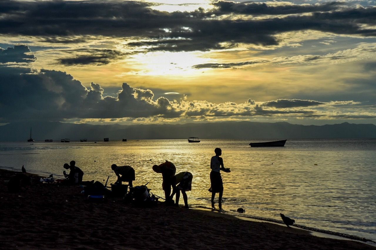 Silhouetted figures on the shore at sunset