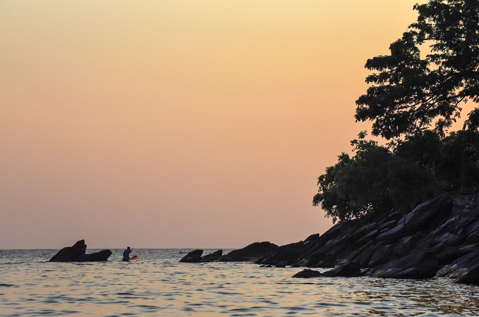 Rocky headland silhouetted at sunset with a figure in the water